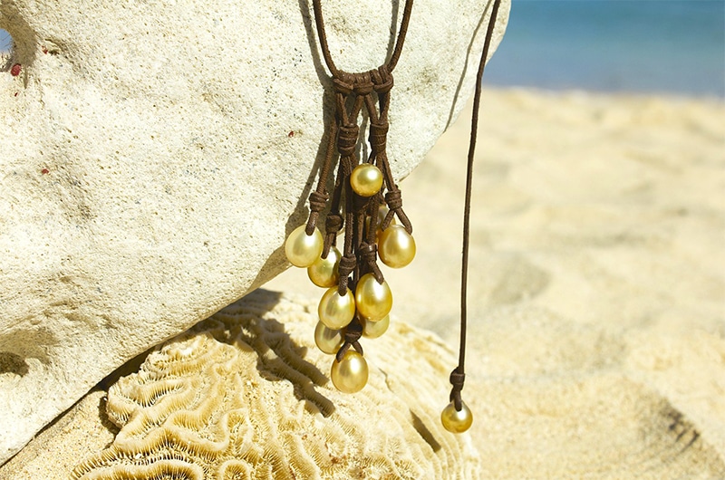 Close view of the cluster necklace with 11 golden South Sea cultured pearls displayed on a rock facing the sea