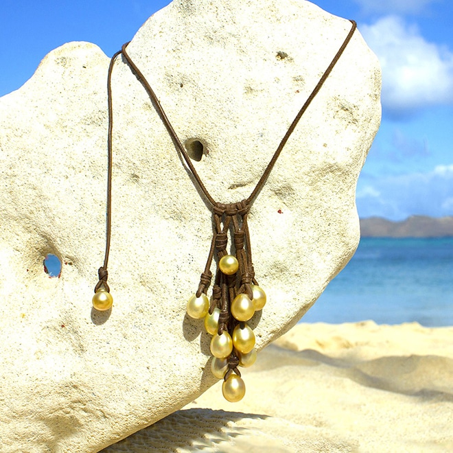 Adjustable leather cluster necklace with 11 golden South Sea cultured pearls displayed on a coral stand at the beach