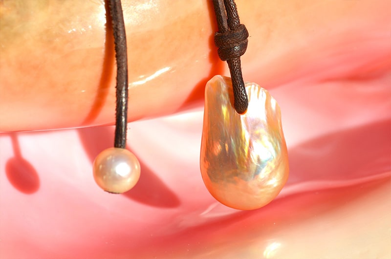 Close-up of the large Fireball pearl and pink freshwater cultured pearl on the necklace displayed on a pink seashell