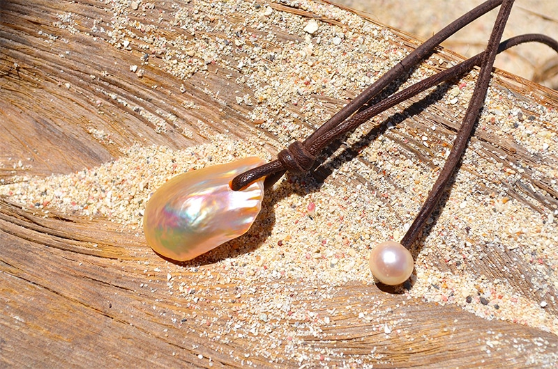 Detail of the large Fireball pearl, pink freshwater pearl and knots on the pendant necklace displayed on wood