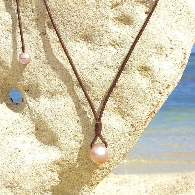 Adjustable leather pendant necklace with two pink freshwater cultured pearls displayed on a coral stand facing the sea