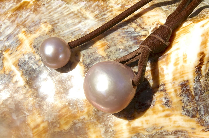 Close-up of the two pink freshwater cultured pearls and knots on the pendant necklace displayed on mother-of-pearl