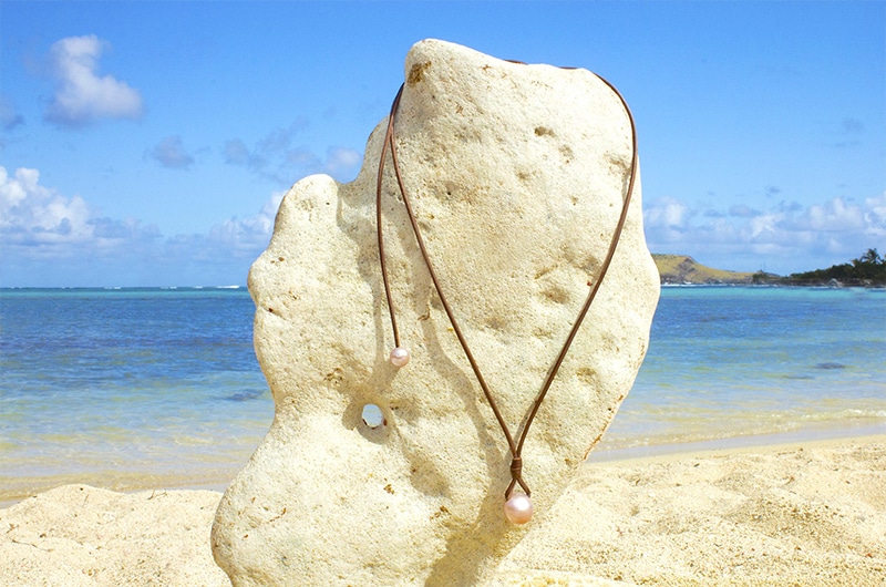 Full view of the adjustable pendant necklace with two pink freshwater cultured pearls displayed on a coral stand at the beach