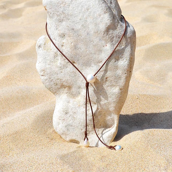 Vue d’ensemble du sautoir ajustable en cuir avec trois perles de culture d’eau douce présenté sur un support corallien à la plage