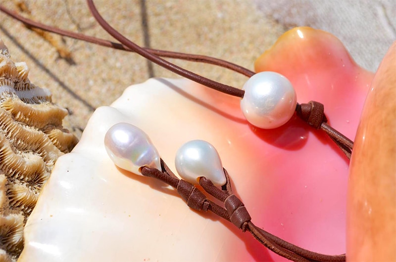 Détail des trois perles de culture d’eau douce et du cuir marron du sautoir présentés sur un coquillage rose