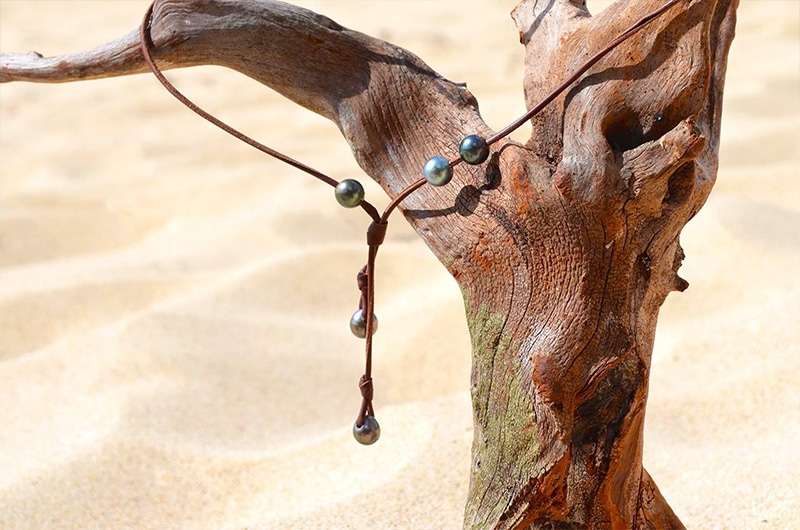 Adjustable long necklace with five Tahitian cultured pearls hanging from driftwood at the beach