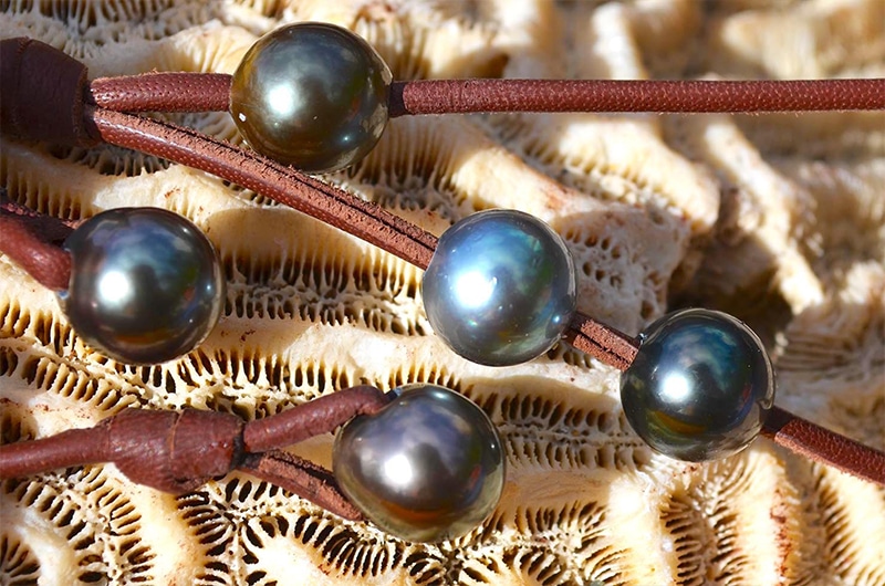 Close-up of the five Tahitian cultured pearls and brown leather on the long necklace displayed on coral