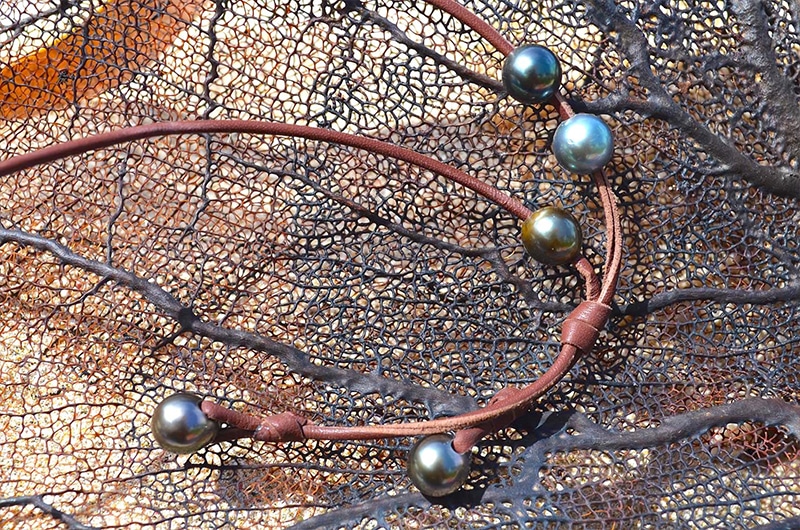Detail of the five Tahitian cultured pearls, knots and brown leather on the long necklace displayed on a dark rock