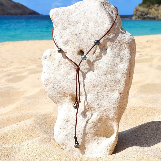 Full view of the adjustable long necklace with five Tahitian cultured pearls displayed on a coral stand at the beach