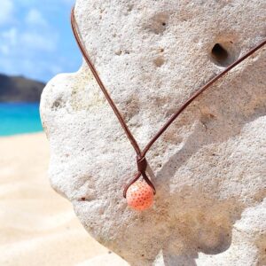 Adjustable leather pendant necklace with a coral element and a Tahitian cultured pearl displayed on a coral stand at the beach