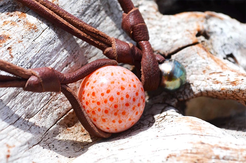 Close-up of the coral element, Tahitian pearl and leather setting on the pendant necklace displayed on driftwood