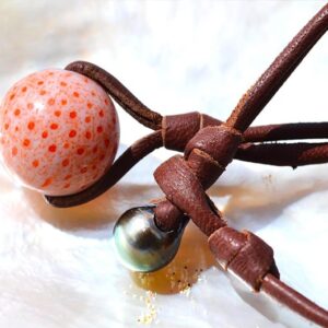 Detail of the coral element, Tahitian cultured pearl and knots on the pendant necklace displayed on mother-of-pearl