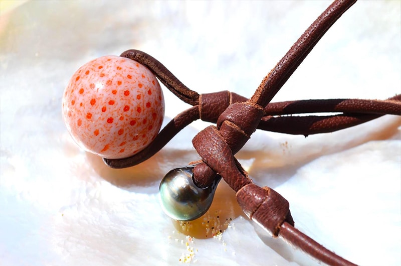 Detail of the coral element, Tahitian cultured pearl and knots on the pendant necklace displayed on mother-of-pearl