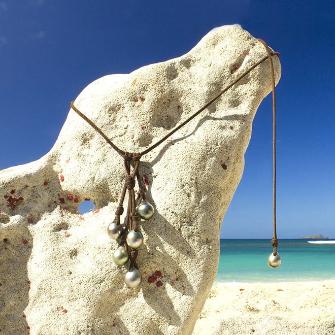 Adjustable leather cluster necklace with five main 10.5 mm Tahitian pearls and one adjustment pearl displayed at the beach