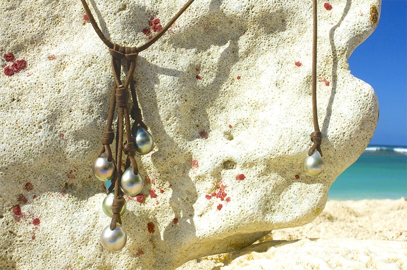 Alternate view of the adjustable cluster necklace with five main 10.5 mm Tahitian pearls displayed on a rock facing the sea