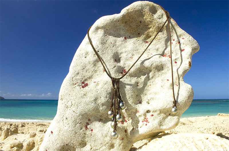 Full view of the cluster necklace with five main 10.5 mm Tahitian pearls displayed on a coral stand facing the sea