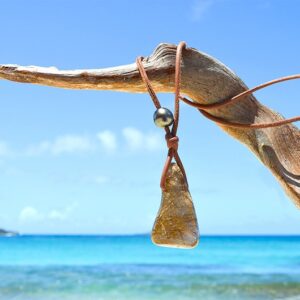 Full view of the rutilated quartz pendant and Tahitian pearls on the necklace hanging from driftwood at the beach