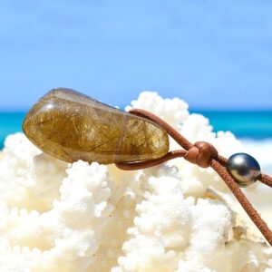 Adjustable leather pendant necklace with rutilated quartz and two Tahitian cultured pearls displayed on coral facing the sea
