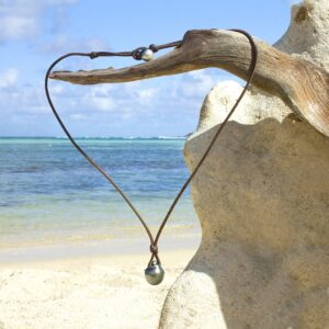 Adjustable leather pendant necklace with two Tahitian cultured pearls displayed on a coral stand at the beach