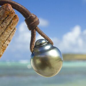 Close-up of the main Tahitian pearl and secondary pearl on the pendant necklace hanging from wood facing the sea