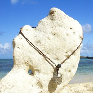 Full view of the leather necklace with an antique Spanish four-reales coin displayed on a coral stand at the beach