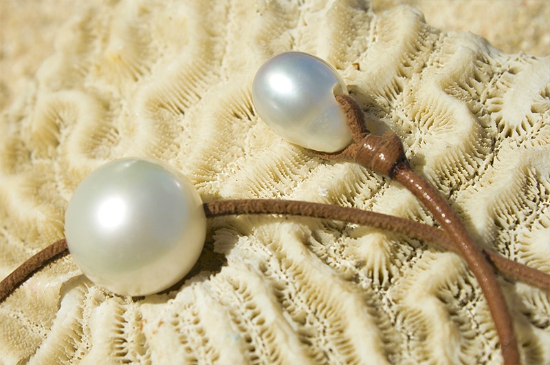 Gros plan sur la perle blanche des mers du Sud de 16 mm, la perle de fermoir et les nœuds du collier présentés sur une nacre