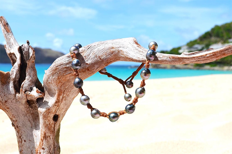 Convertible jewelry with 17 Tahitian cultured pearls arranged in a loop on driftwood at the beach