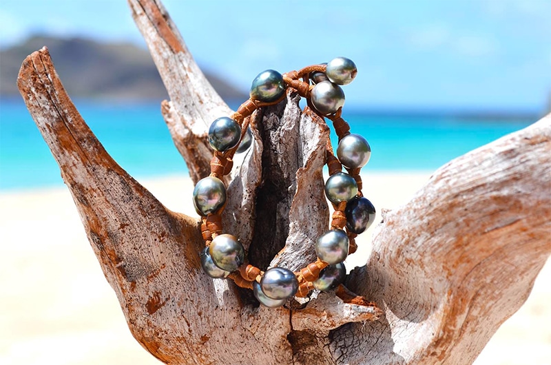 Detail of the 17 Tahitian cultured pearls and leather setting of the necklace bracelet displayed on driftwood