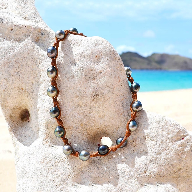 Convertible jewelry worn as a choker necklace or double-wrap bracelet with 17 Tahitian cultured pearls displayed on coral at the beach