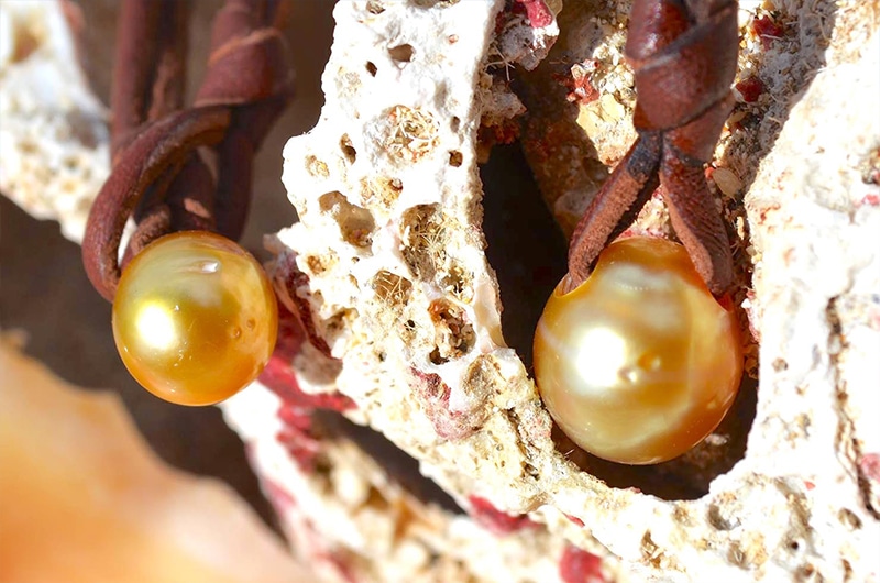 Vue rapprochée des deux perles dorées des mers du Sud et du cuir marron du collier pendentif présentés sur du bois