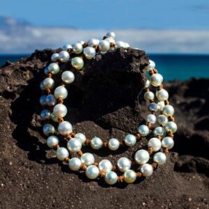 Sautoir en cuir avec 70 perles de culture blanches des mers du Sud présenté enroulé sur une roche sombre face à la mer