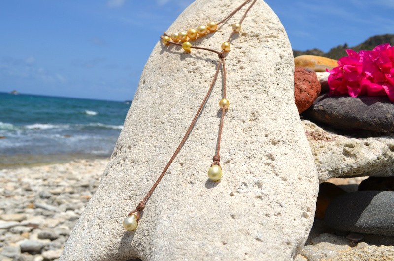 Alternate view of the long necklace with 12 golden South Sea pearls displayed on a rock at the beach