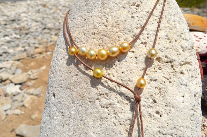 Close-up of the golden South Sea pearls and brown leather ends of the long necklace on a rock