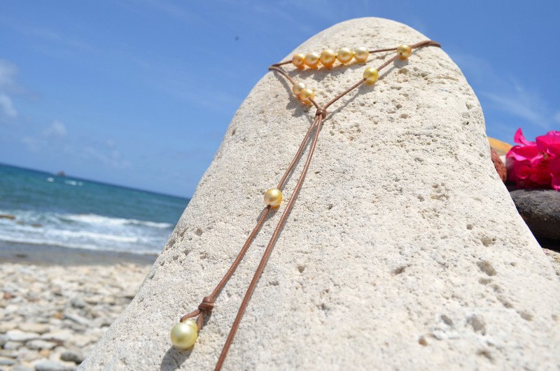 Adjustable long necklace with 12 golden South Sea pearls displayed fully extended on coral facing the sea