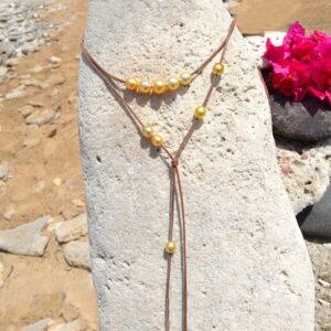 Adjustable leather long necklace with 12 golden South Sea cultured pearls displayed on a rock at the beach