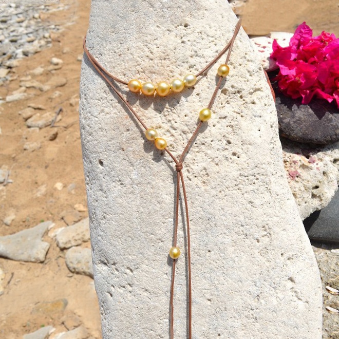 Adjustable leather long necklace with 12 golden South Sea cultured pearls displayed on a rock at the beach