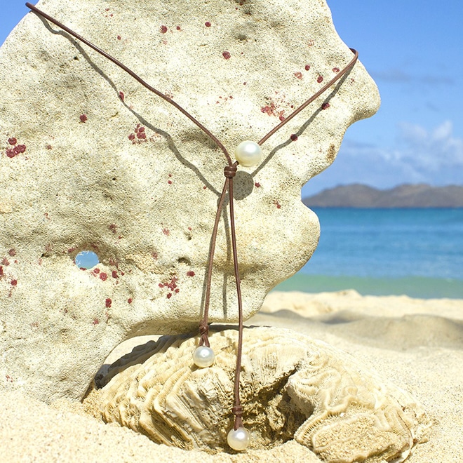 Adjustable leather long necklace with three white South Sea cultured pearls displayed on coral at the beach