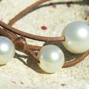Close-up of the three white South Sea pearls and brown leather of the long necklace displayed on coral