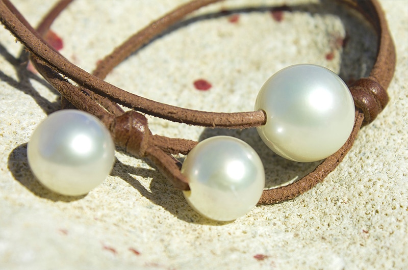 Close-up of the three white South Sea pearls and brown leather of the long necklace displayed on coral