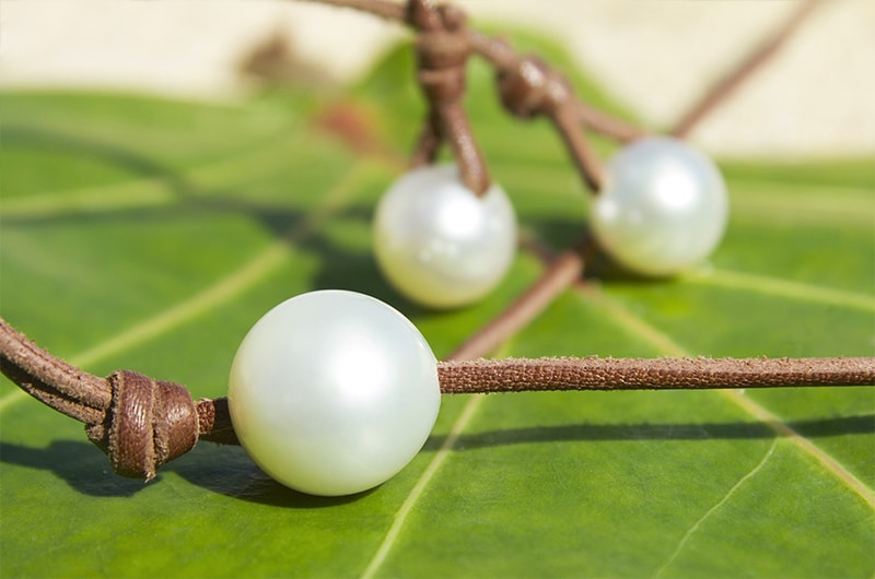 Detail of the three white South Sea cultured pearls and knots of the long necklace displayed on a green leaf
