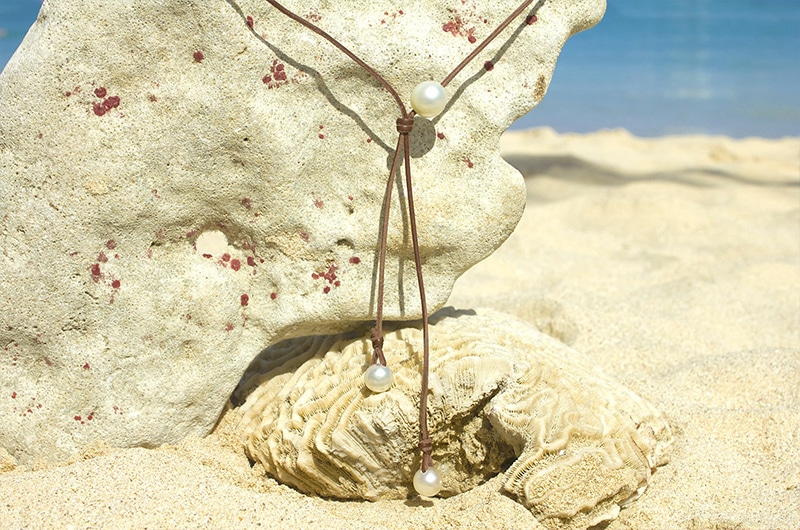 Full view of the adjustable long necklace with three white South Sea pearls displayed on coral at the beach