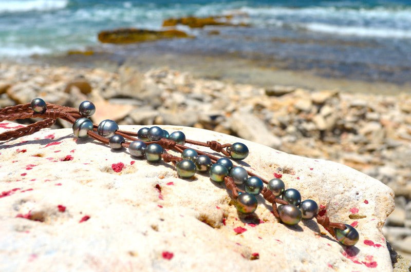 Close-up of the 25 Tahitian cultured pearls and braided leather of the necklace arranged on a rock at the beach