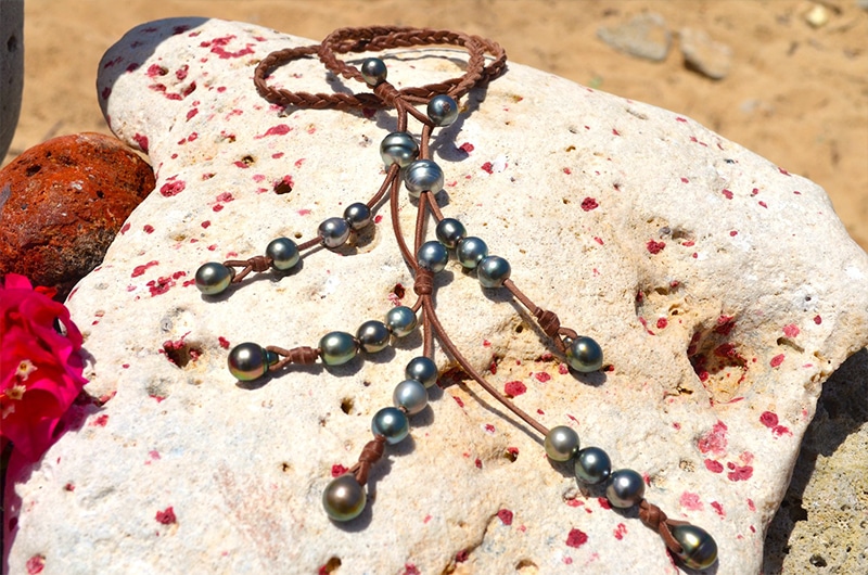 Braided necklace with 25 Tahitian cultured pearls displayed fully extended with its leather ends on a rock