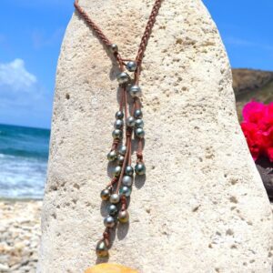 Collier en cuir tressé avec 25 perles de culture de Tahiti présenté verticalement sur un support corallien face à la mer
