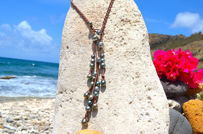 Braided leather necklace with 25 Tahitian cultured pearls displayed vertically on coral facing the sea