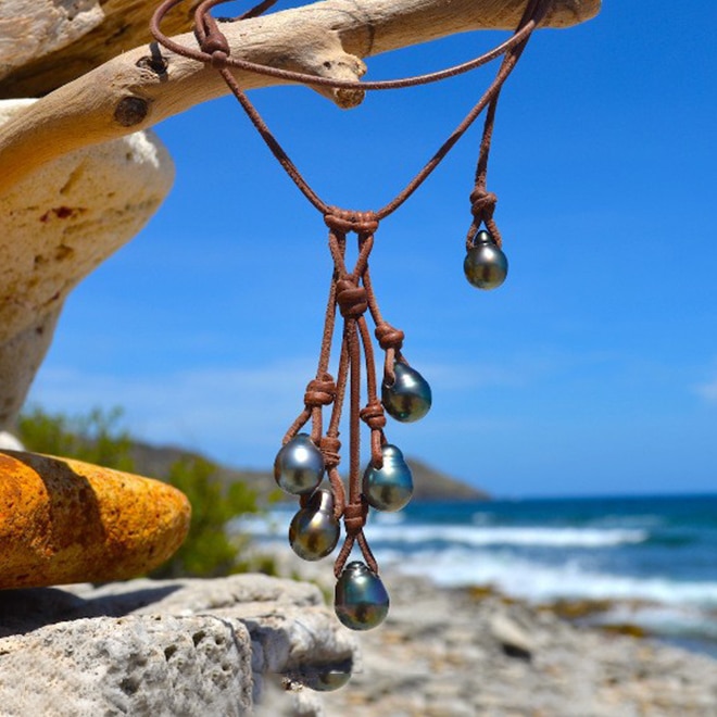 Adjustable leather cluster necklace with six Tahitian cultured pearls displayed hanging in front of the sea