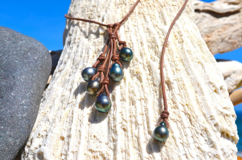 Close-up of the six Tahitian cultured pearls and leather knots of the cluster necklace displayed on driftwood
