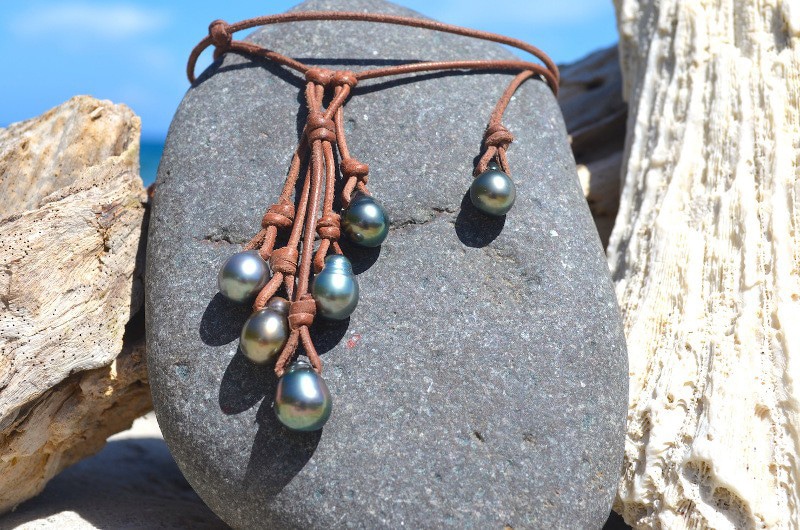 Alternate view of the cluster necklace with six Tahitian cultured pearls displayed on a dark rock at the beach