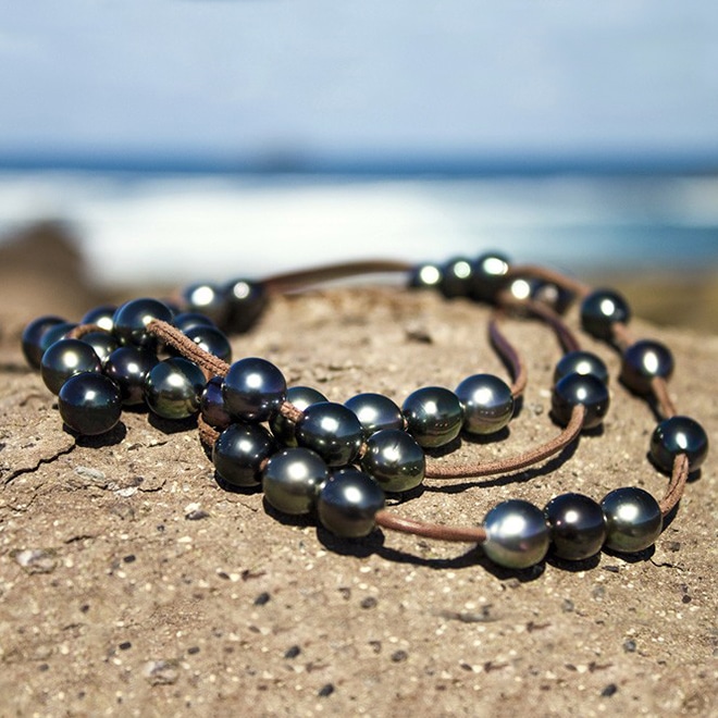 Leather long necklace with 50 semi-baroque Tahitian cultured pearls displayed coiled on a rock facing the sea