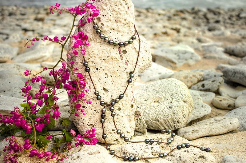 Full view of the convertible leather long necklace with 50 semi-baroque Tahitian cultured pearls displayed on a rock among pink flowers
